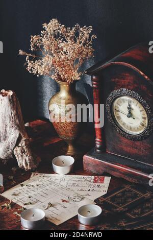 Cartes postales vintage avec écriture cursive en italique sur une table en bois sombre. Ambiance rustique avec bougies, vieille horloge antique, vase en laiton Banque D'Images