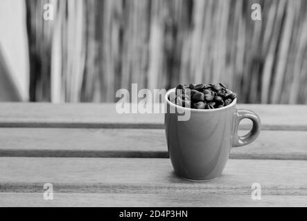 Gros plan en niveaux de gris de deux tasses complètes avec café rôti haricots sur une table en bois Banque D'Images