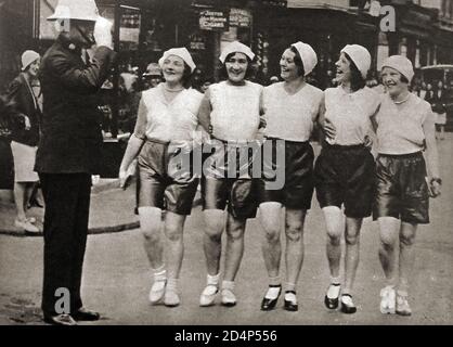 1930 les vêtements de sport britanniques étaient destinés aux pantalons de plage et aux chapeaux de style marin américain. Autre article de mode populaire pour les femmes, était le port de shorts, en particulier pour la randonnée, une tendance reprise par les films parlants. Ces jeunes femmes portent un short, une idée importée de la Côte d'Azur, mais à cette occasion elles marchent dans les rues de la ville jusqu'à l'apparatapprobation d'un Bobby britannique (policier) Banque D'Images