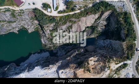 Vue aérienne de la carrière minière en plein ciel avec de nombreuses machines en service, des pelles hydrauliques et des foreuses. Vue panoramique sur la fosse en pierre. Banque D'Images