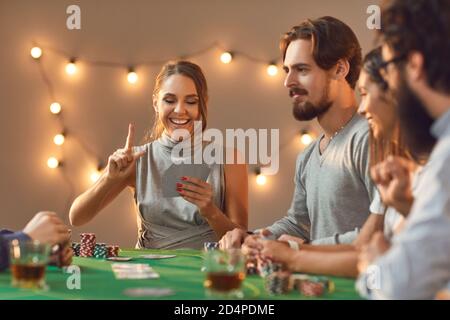 Une jeune femme heureuse tient le doigt comme elle a de la chance main dans le jeu de poker avec des amis Banque D'Images