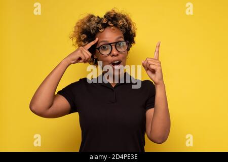 Jeune femme africaine aux cheveux bouclés ayant l'idée pointant avec doigt vers le haut Banque D'Images