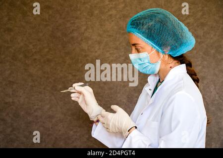 Portrait des médecins avec masque, gant et uniforme et lame chirurgicale à portée de main sur fond gris. Banque D'Images