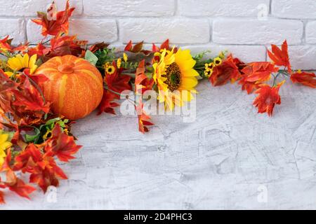 Belle nature automnale encore avec des tournesols, des fleurs rouges-jaunes, des feuilles d'automne et de la citrouille orange sur fond de mur de briques blanches. Vue de face. Concept d'automne avec citrouille et fleurs. Espace de copie mise au point douce. Banque D'Images