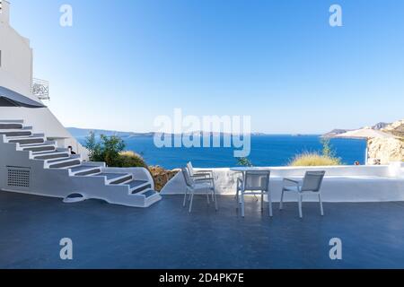 Quatre chaises blanches avec table blanche sur la terrasse blanche avec vue sur la mer bleue et la caldeira par jour ensoleillé, sans personne. Oia, île de Santorin, Grèce Banque D'Images