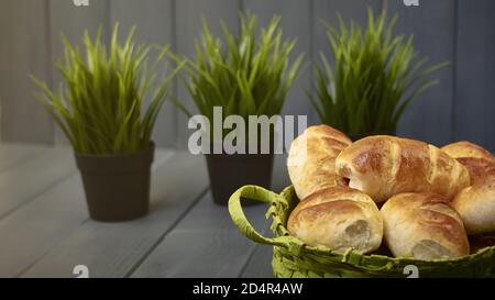 Pain au lait. Bonbons typiques cuits au levain et faits maison dans un panier en osier sur une table en bois gris et des plantes vertes Banque D'Images