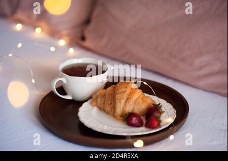 Tasse de thé noir frais restant sur papier livre ouvert pendant Noël lumières incandescentes gros plan. Bonjour. Petit déjeuner. Saison des vacances d'hiver. Banque D'Images