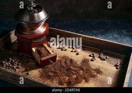 Moulin à café manuel nostalgique, grains torréfiés et café moulu sur plateau en bois rustique, fond sombre avec espace de copie, mise au point sélectionnée, petit rayon Banque D'Images