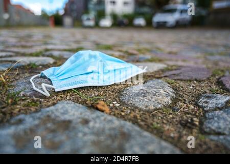 Masque chirurgical contre l'infection par le coronavirus et le covid-19 jeté sur une place pavée dans la ville, espace de copie, foyer sélectionné, très n Banque D'Images