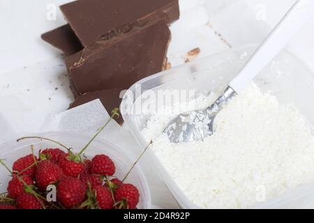 Flocons de noix de coco et crème dans un récipient. À proximité se trouvent les framboises et les morceaux de chocolat. Levington gâteau, étapes de préparation. Banque D'Images