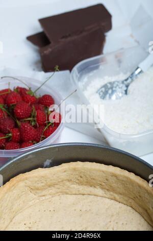 Génoise dans un plat à pâtisserie. Flocons de noix de coco et crème dans un récipient. À proximité se trouvent les framboises et les morceaux de chocolat. Levington gâteau, étapes de la préparation Banque D'Images
