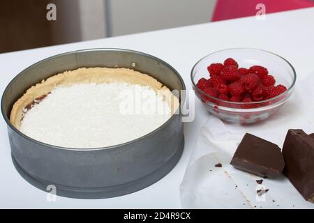 Flocons de noix de coco dans un biscuit avec ganache au chocolat. À proximité se trouvent les framboises avec des morceaux de chocolat. Levington gâteau, étapes de préparation. Banque D'Images