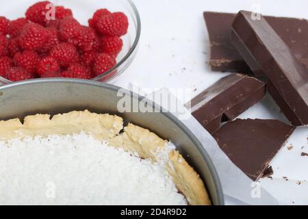 Flocons de noix de coco dans un biscuit avec ganache au chocolat. À proximité se trouvent les framboises avec des morceaux de chocolat. Levington gâteau, étapes de préparation. Banque D'Images