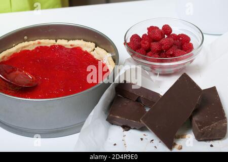 Une femme couvre des flocons de noix de coco dans un gâteau éponge avec ganache au chocolat et gelée de framboise. À proximité se trouvent les framboises avec des morceaux de chocolat. Levington Banque D'Images