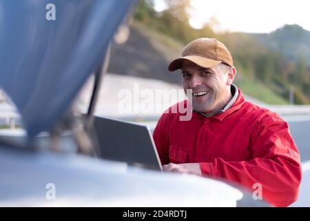 Beau mécanicien d'automobile ou travailleur d'assistance routière en uniforme la réparation de moteur de la voiture cassée sur la route Banque D'Images