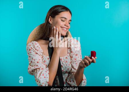 Belle jeune femme tenant une petite boîte à bijoux avec proposition anneau de diamant sur fond de mur bleu. Madame souriante, elle est heureuse d'obtenir le présent Banque D'Images