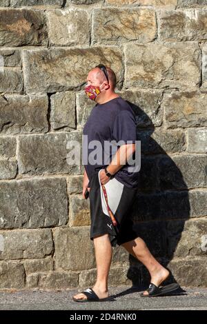 Ellicott City, MD, USA 10/07/2020: Un homme blanc portant des vêtements décontractés d'été marche sur le côté à pied près d'un mur de briques portant un rouge skins football Banque D'Images