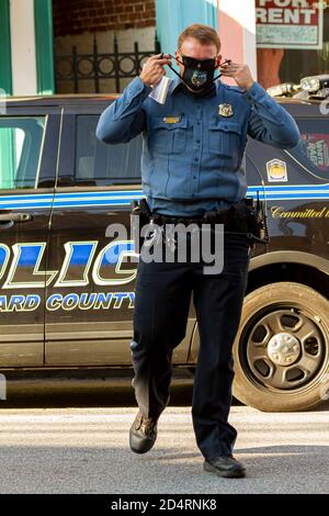 Ellicott City, MD, USA 10/07/2020: Un jeune officier de police de race blanche traverse la rue. Il met son masque noir pendant qu'il marche Banque D'Images