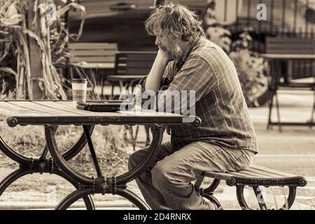 Ellicott City, MD, USA 10/07/2020: Image en noir et blanc d'un vieil homme inconnu assis seul sur un banc de pique-nique, il semble inquiet et réfléchi avec humour Banque D'Images