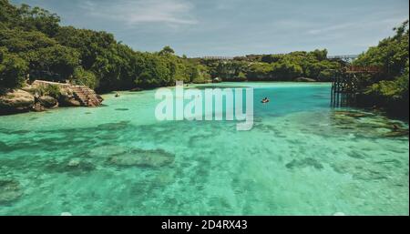 Gros plan les gens nagent à l'eau claire de cristal turquoise du lac de Weekuri. Site touristique dans la forêt tropicale verte avec haut pont. Des vacances d'été magiques dans le paradis tropical de l'île de Sumba, Indonésie Banque D'Images
