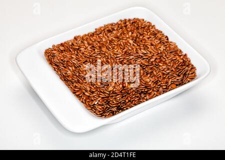 Lin, graines de lin. Lin, dans un récipient blanc. Arrière-plan blanc. Cent grammes de graines de lin moulues fournit environ 534 calories, 41 grammes de graisse, Banque D'Images