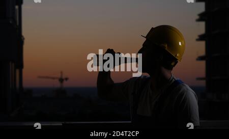 Ouvrier de construction buvant de la bière dans un casque. Banque D'Images