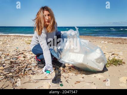 Une jeune femme nettoie la plage et montre des couvercles de bouteille en plastique en main Banque D'Images