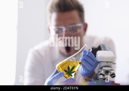 Homme dans des lunettes dans des gants en caoutchouc tient flacon avec jaune liquide dans un laboratoire chimique Banque D'Images