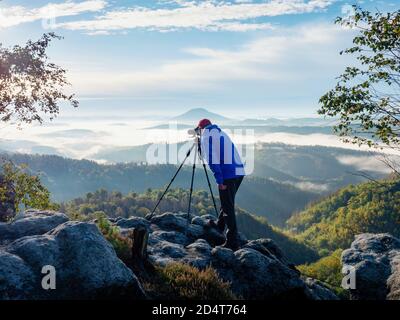 Photographe cadrage de la scène dans le viseur. L'homme utilise l'appareil photo sur trépied pour prendre des photos de paysages de montagnes brumeuses. Détendez-vous sur le concept de vacances Banque D'Images