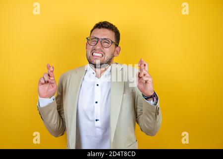 Jeune homme d'affaires beau portant le costume sur fond jaune isolé gesturant le doigt se croise en souriant avec espoir Banque D'Images