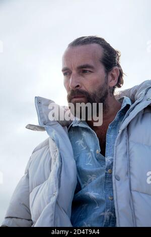 Homme barbu dans la veste Puffa contre le ciel Banque D'Images