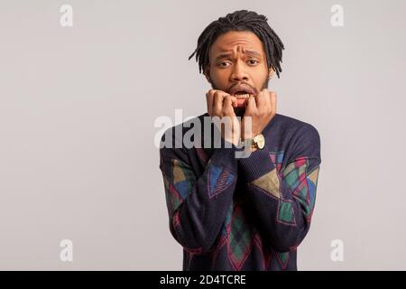 Peur choqué homme africain dans le sweat-shirt à la mode avec des dreadlocks mordant ses ongles, déçu de mauvaises nouvelles, nerveux et peur, désespoir. Intérieur Banque D'Images