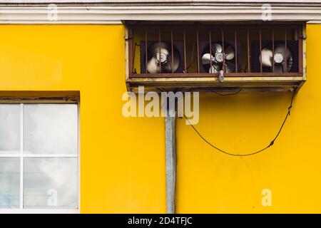 Ancienne climatisation rouillée près d'une fenêtre en plastique. Mur jaune vieilli avec rayures et fissures. Сables depuis le climatiseur. Fils sur Fig Banque D'Images