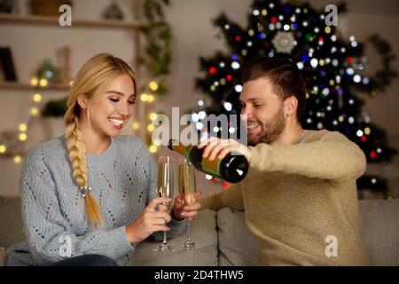 Un jeune couple boit du champagne, célébrant ensemble le nouvel an à la maison Banque D'Images