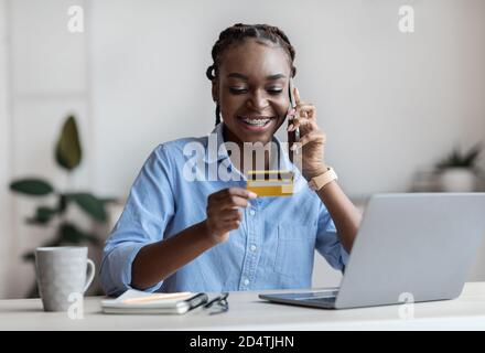 Paiements mobiles. Femme d'affaires tenant une carte de crédit et parlant au téléphone cellulaire au bureau Banque D'Images