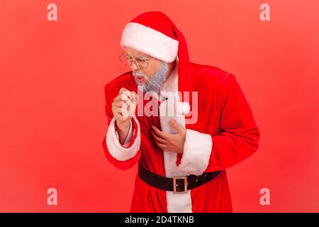 Portrait d'un homme malade âgé à barbe grise en costume du père noël et de lunettes toussant le poing tenant une autre main sur la poitrine, risque de pneumonie. JE Banque D'Images