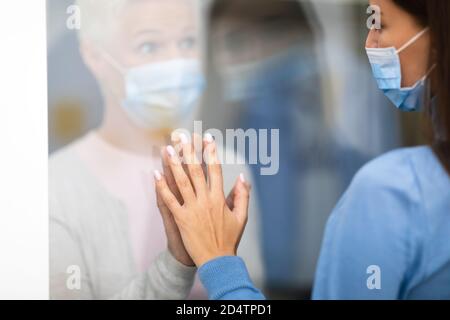 Une femme infectée par Covid-19 touche la main de sa fille par la porte de l'hôpital Glass Banque D'Images