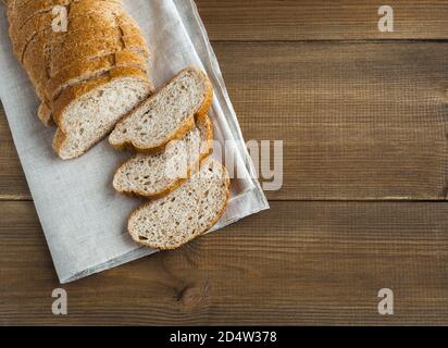 Un pain de blé blanc avec son sur une serviette en lin. Plusieurs coupes ont été coupées. Pose plate avec place pour le texte sur fond marron en bois. Banque D'Images