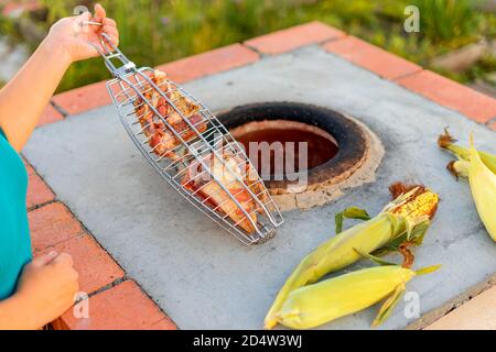 Les mains d'une femme caucasienne cuisent de la viande en tandoor. Brochettes dans la tandoor. Cuisson du kebab de viande dans un tandoor. Maïs. Le concept de la cuisine. Mise au point sélective. Concentrez-vous sur les morceaux de viande. Banque D'Images