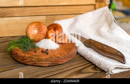 Sur une ancienne table en bois de grunge se trouve une planche à découper avec des champignons de calotte de lait de safran et des ingrédients pour les saler: Sel, aneth, pois de poivre noir. À côté il y a une serviette et un couteau. Vue rapprochée. Faible profondeur de champ. Banque D'Images