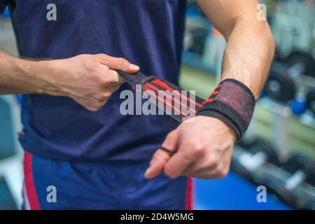 Un homme dans la salle de gym en ajustant ses bracelets avant de soulever. Presse pour établi. Les bracelets se rapprochent. Banque D'Images