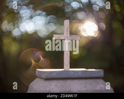Petite croix catholique en bois sur un piédestal en pierre avec un arrière-plan agréable et une réflexion inhabituelle. Banque D'Images