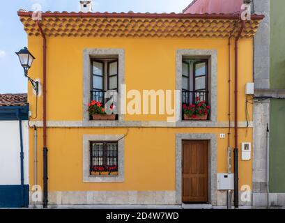 Maison espagnole traditionnelle. Ancien bâtiment restauré, façade peinte en jaune. Fenêtres et balcon encadrés de pierre grise. Porte en bois. Géraniums rouges déc Banque D'Images