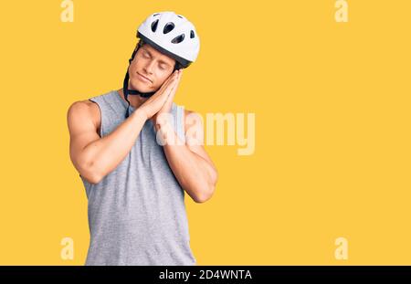 Jeune homme beau portant un casque de vélo dormant fatigué rêvant et posant avec les mains ensemble tout en souriant avec les yeux fermés. Banque D'Images
