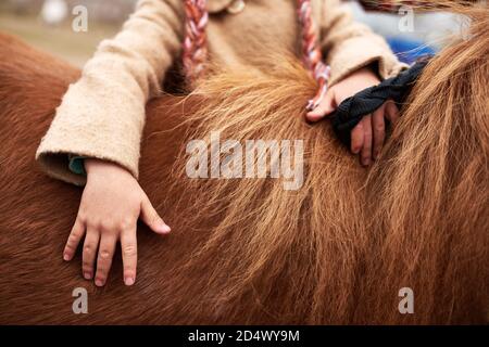 Photo horizontale d'une petite fille méconnue touchant son poney de châtaignier Banque D'Images