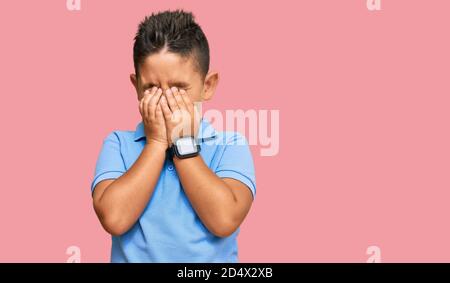 Petit garçon hispanique enfant portant des vêtements décontractés frottant les yeux pour la fatigue et les maux de tête, l'expression de sommeil et de fatigue. Problème de vision Banque D'Images