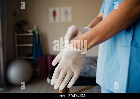 infirmière féminine mettant des gants chirurgicaux se préparant à un rendez-vous avec malade debout en clinique Banque D'Images