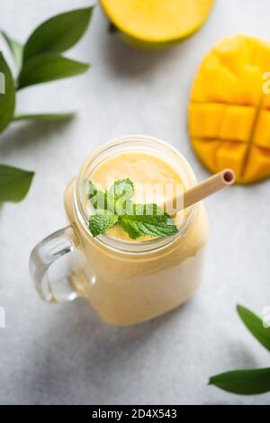 Smoothie à la mangue, lassi à la mangue ou cocktail dans un pot en verre avec paille de bambou sur fond de béton gris Banque D'Images