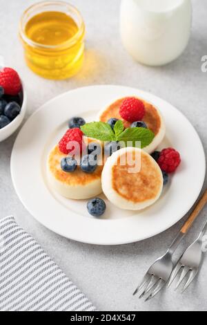 Beignets de fromage cottage Syrniki servi avec des baies d'été et du miel. Cuisine russe et ukrainienne Banque D'Images