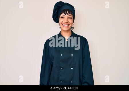 Belle femme brunettte portant un uniforme de cuisinier professionnel avec un sourire heureux et frais sur le visage. Personne chanceux. Banque D'Images